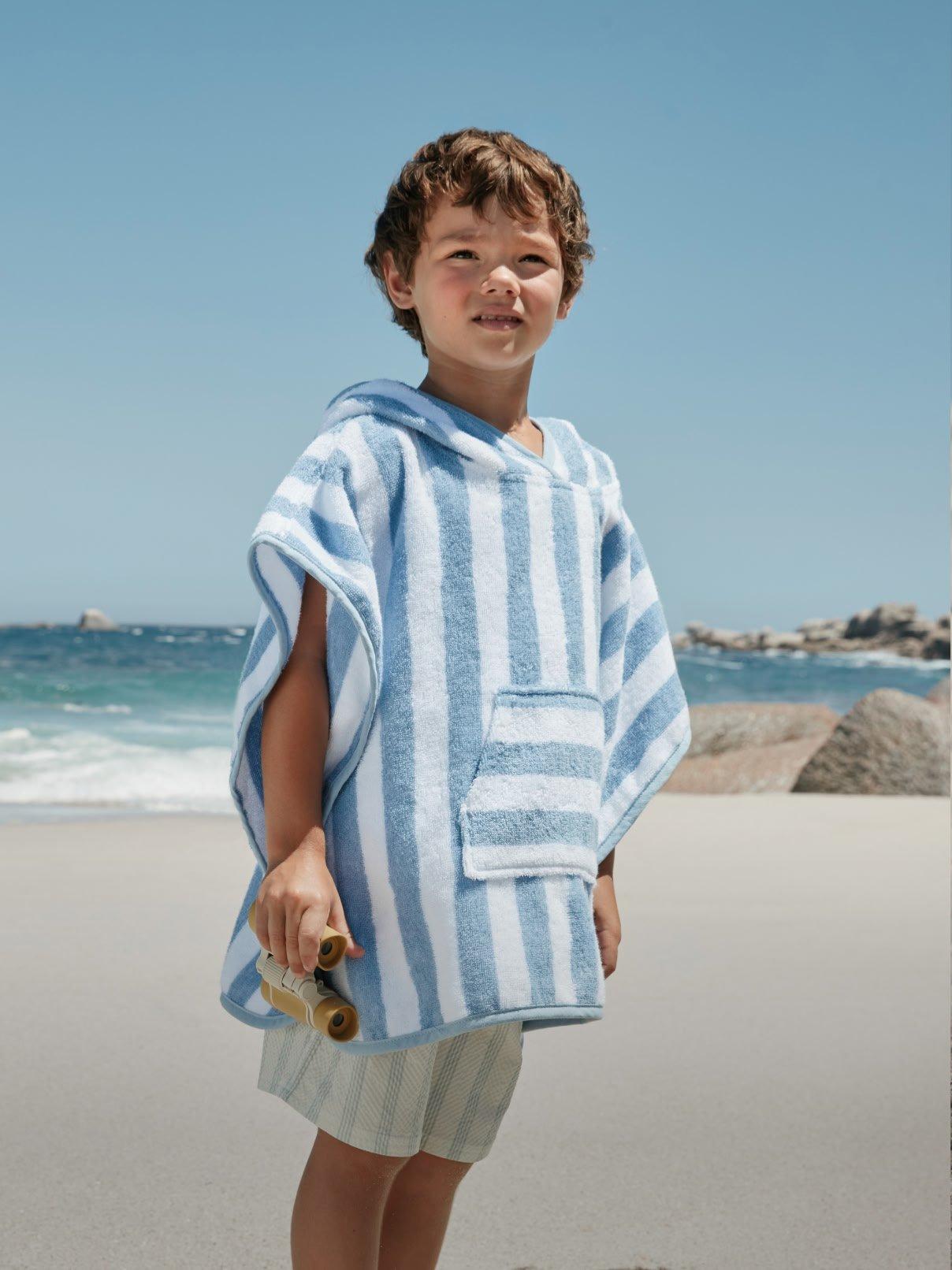 a young boy standing on a beach holding a skateboard