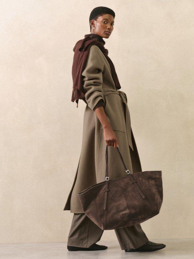 a woman in a trench coat holding a brown bag