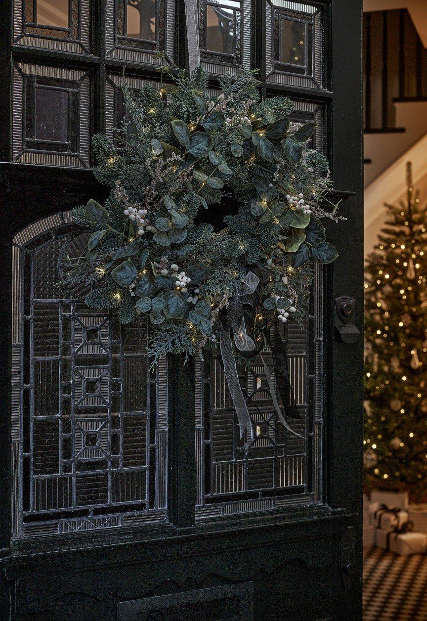 a wreath on the front door of a house with a christmas tree in the background