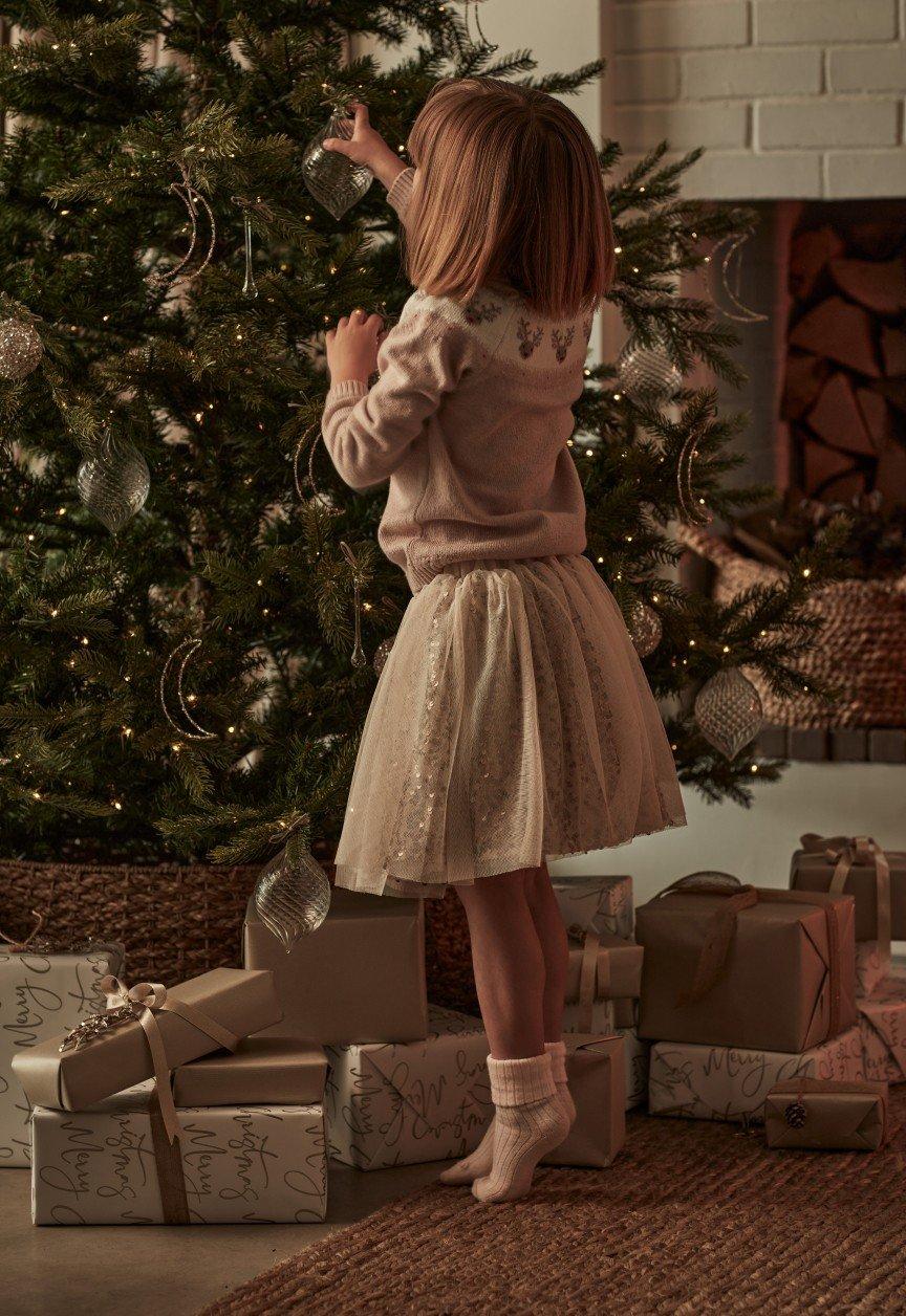 a little girl decorating a christmas tree in a living room