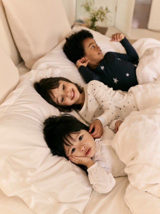 three children laying in bed together on a white bed