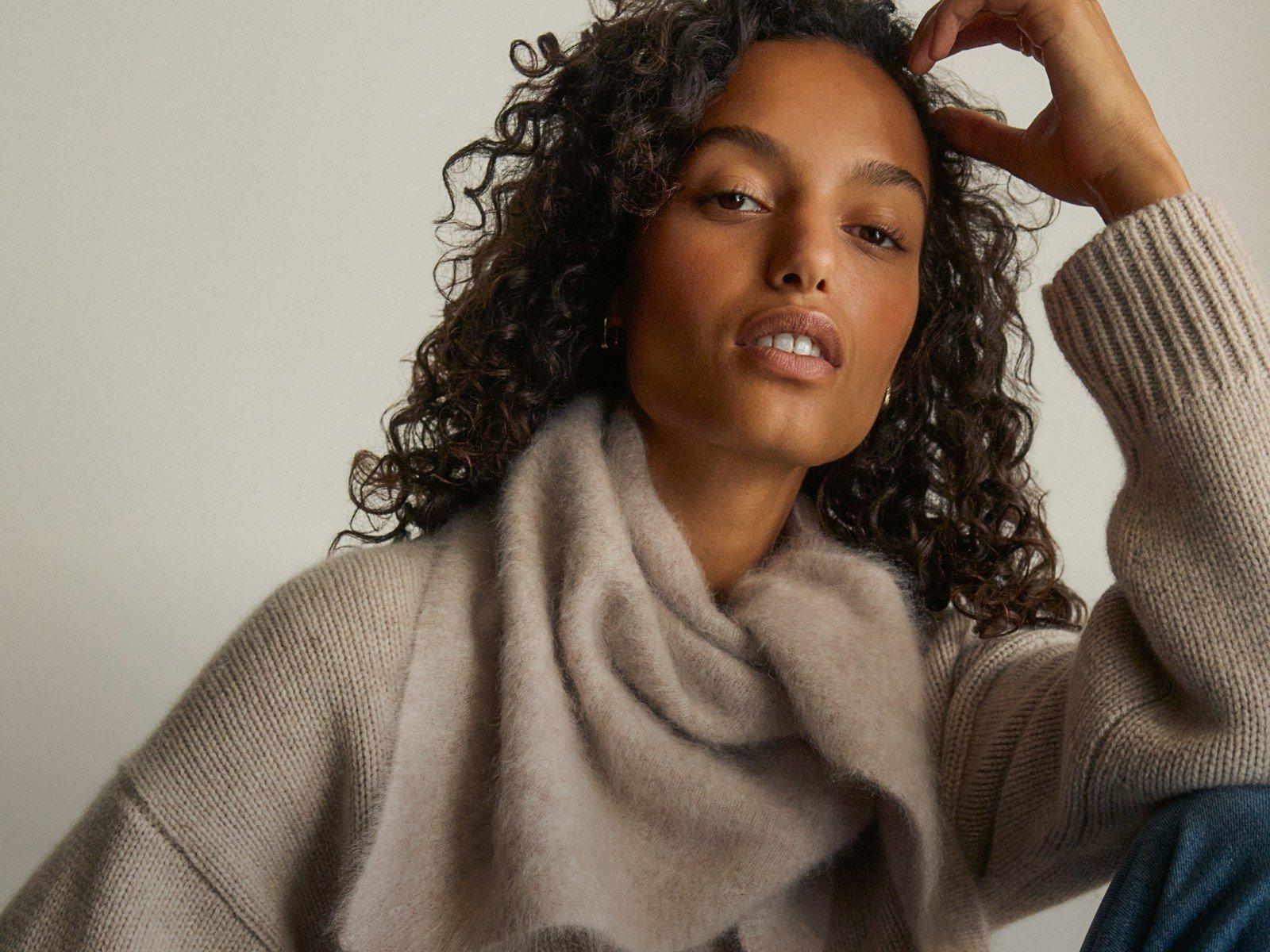 a woman with curly hair sitting on a chair with her hand on her head