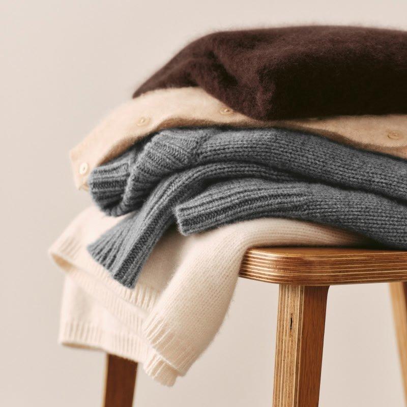 a stack of sweaters on a wooden stool against a white background