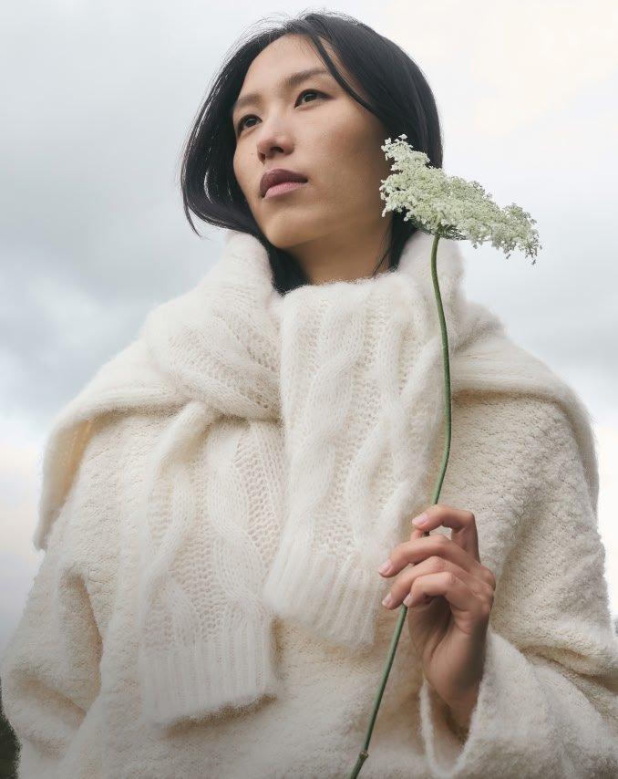 a woman in a white sweater holding a flower in her hand