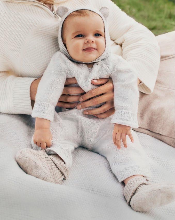 a woman holding a baby in a white outfit on a blanket