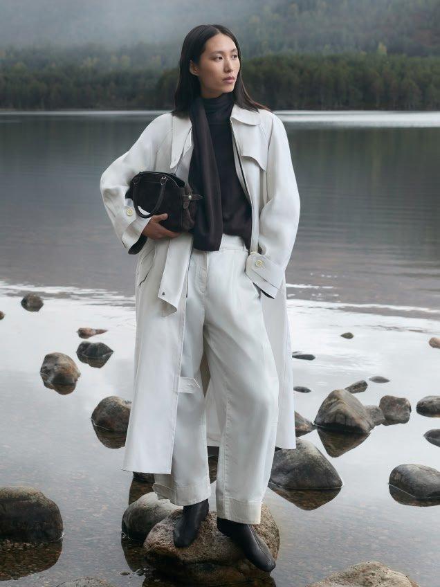 a woman in white coat standing on rocks near water
