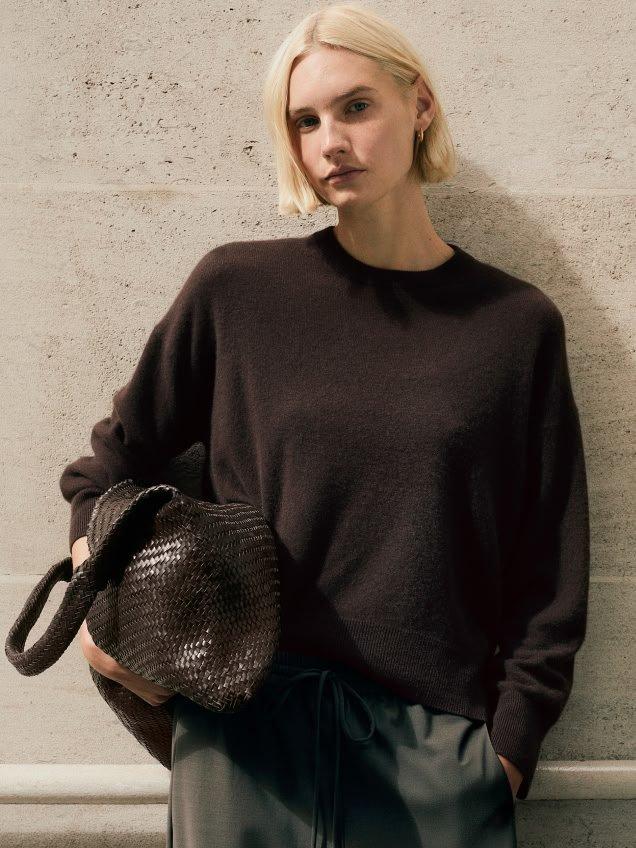 a woman in a sweater and pants leaning against a wall