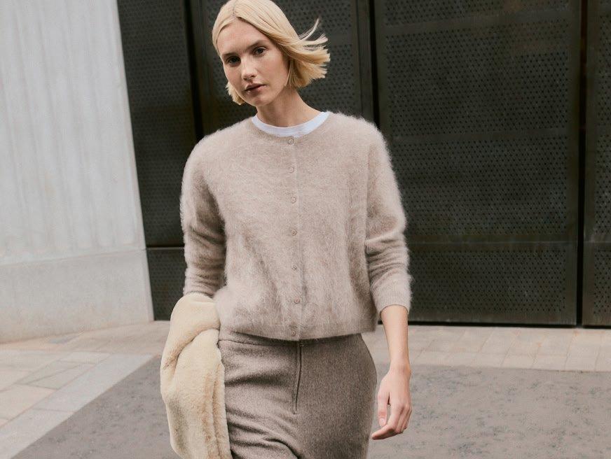 a woman in a beige sweater and skirt walking down the street