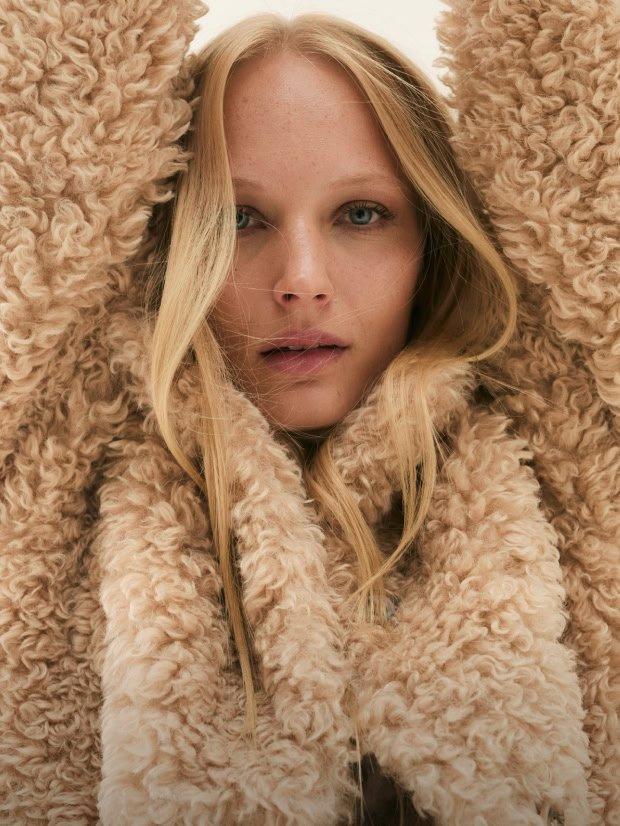 a woman with long blonde hair wearing a fluffy coat