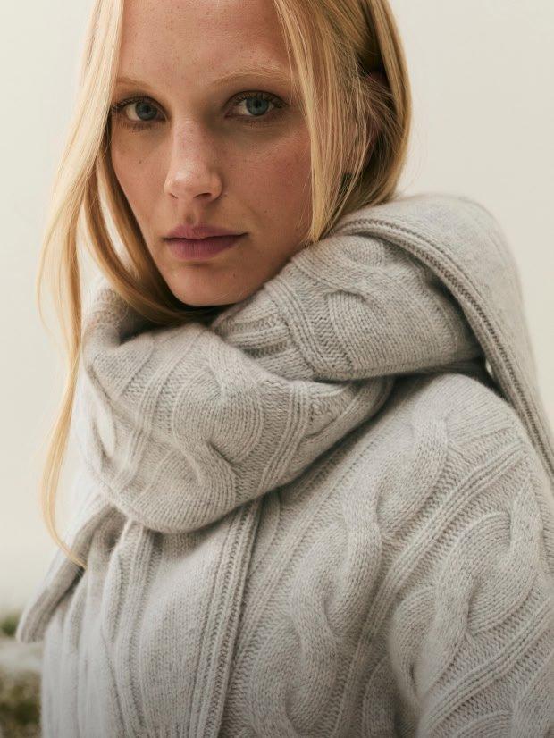 a woman in a white sweater and scarf standing in front of a building
