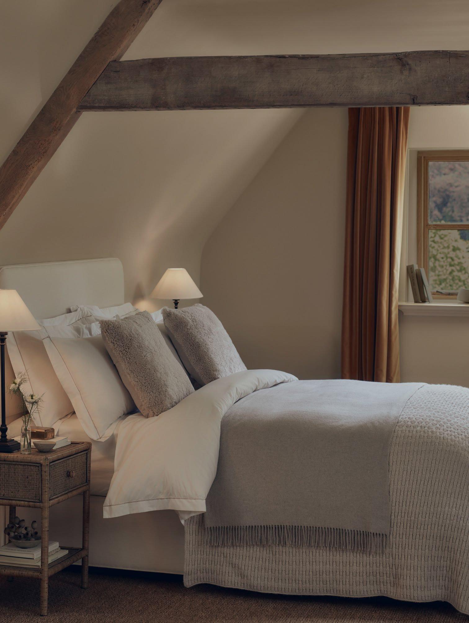 a bed with a white comforter and pillows in a room with a window
