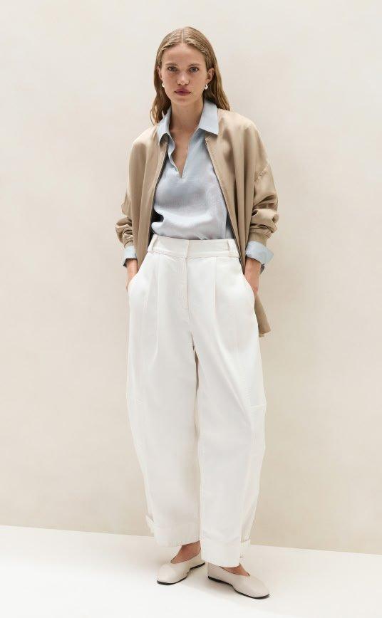 a woman in a white sweater and pants standing against a wall