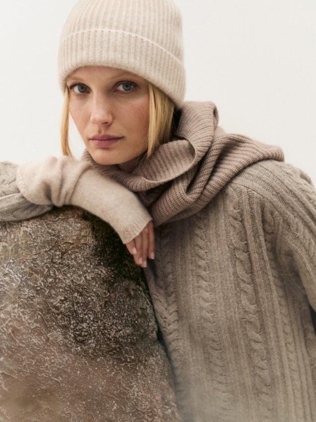 a woman in a hat leaning against a rock with her arms crossed