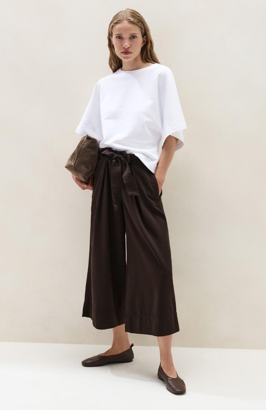 a woman in a white sweater and pants standing against a wall