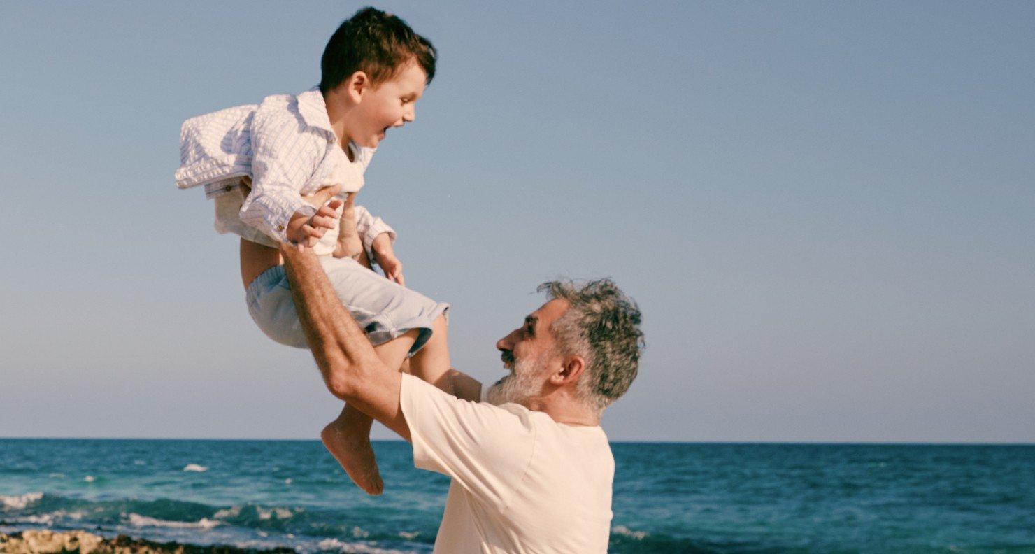 a man holding a child in the air by the beach