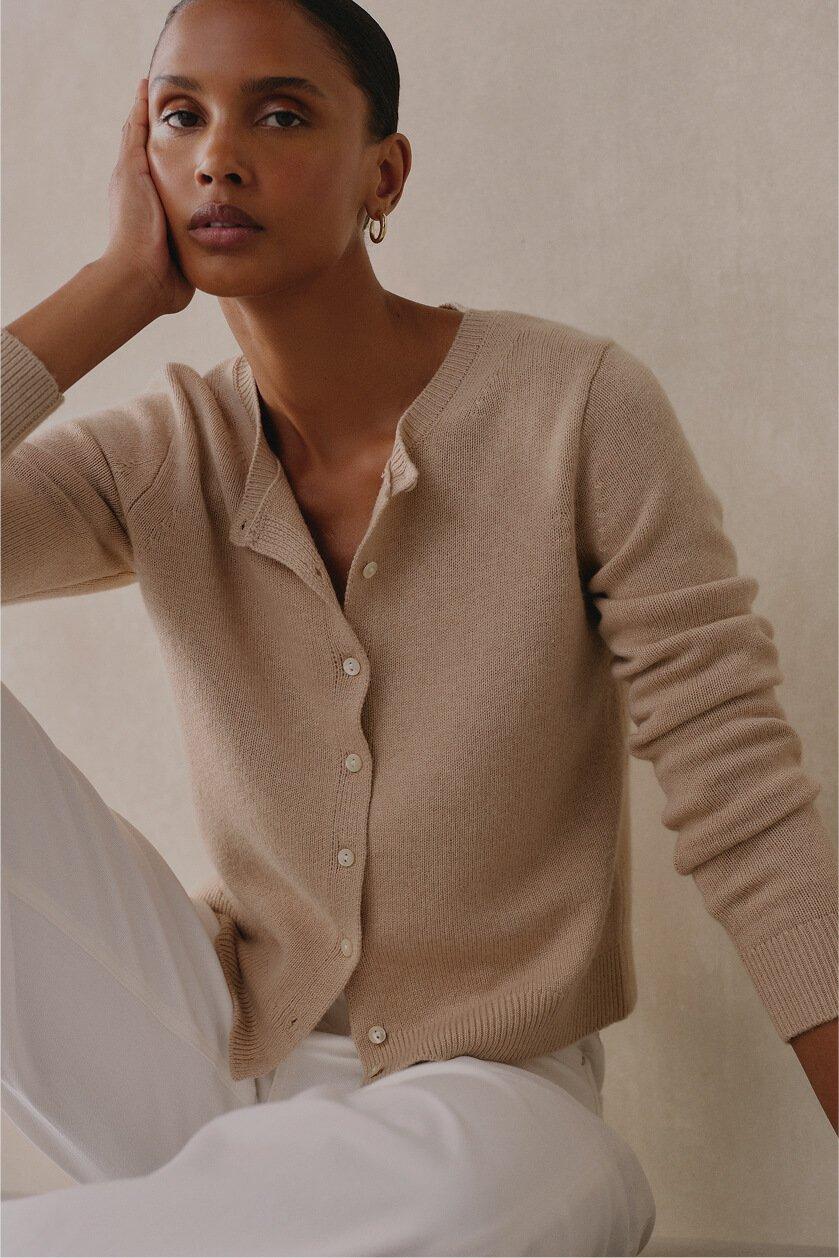a woman in a tan cardigan sweater and white pants
