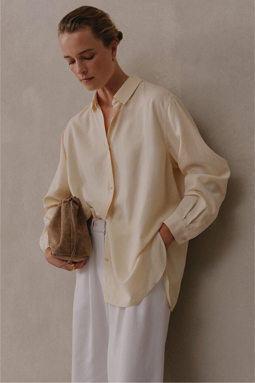 a woman in white pants and a beige shirt holding a purse