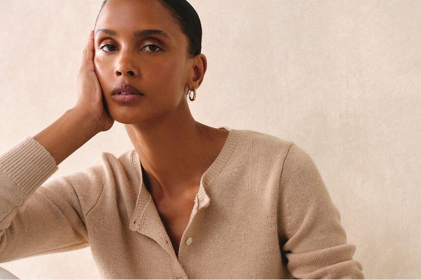 a woman in a beige sweater leaning on her hand