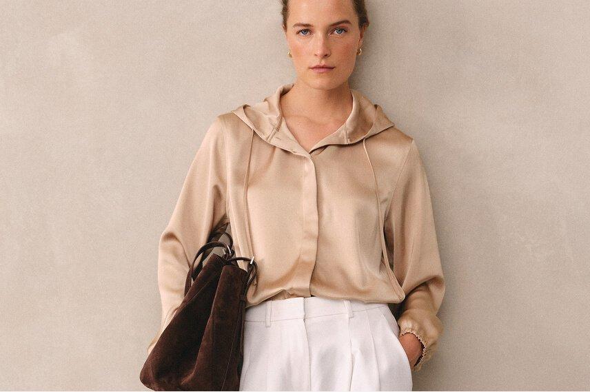 a woman in a white shirt and white pants holding a brown bag