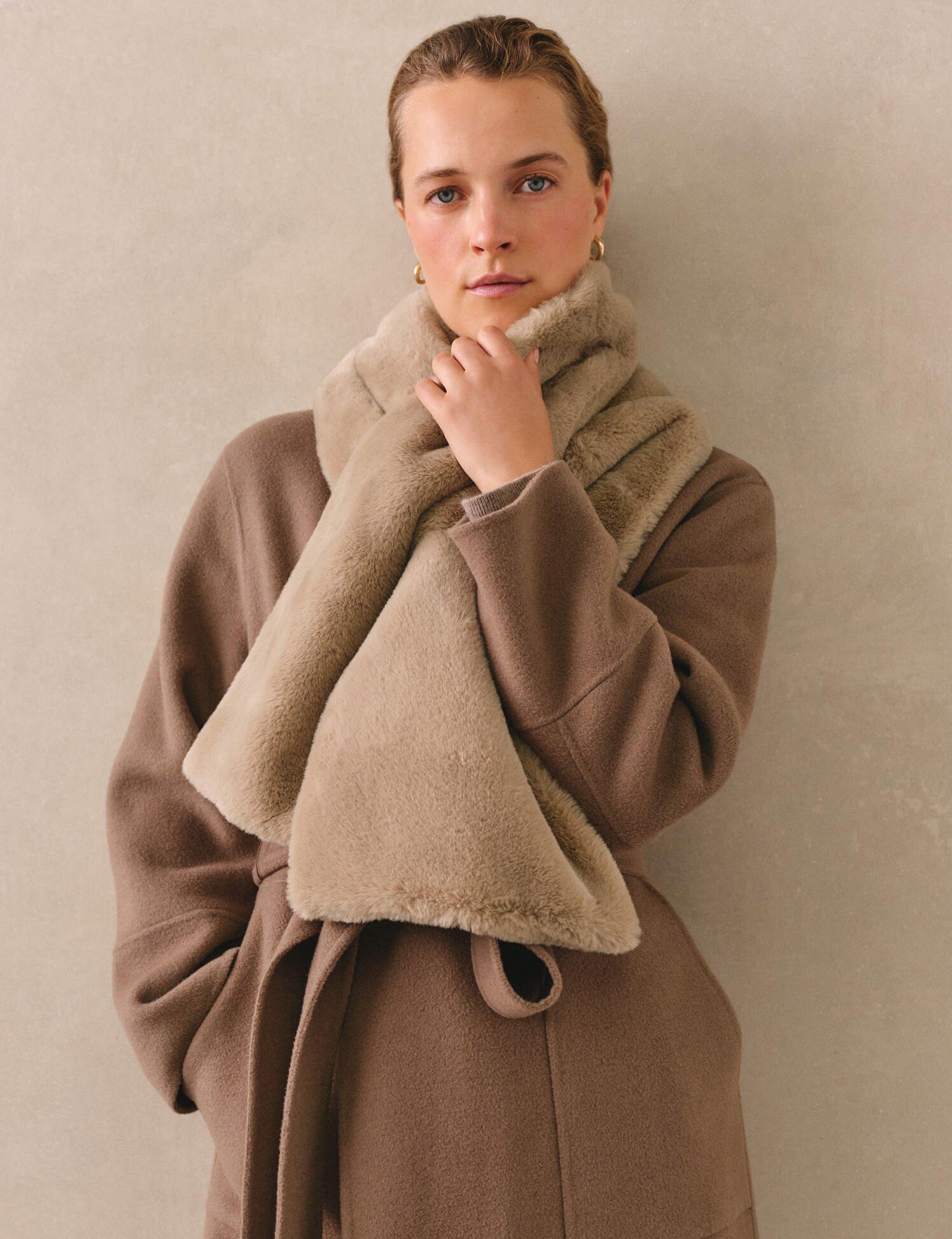 a woman in a coat and scarf leaning against a wall