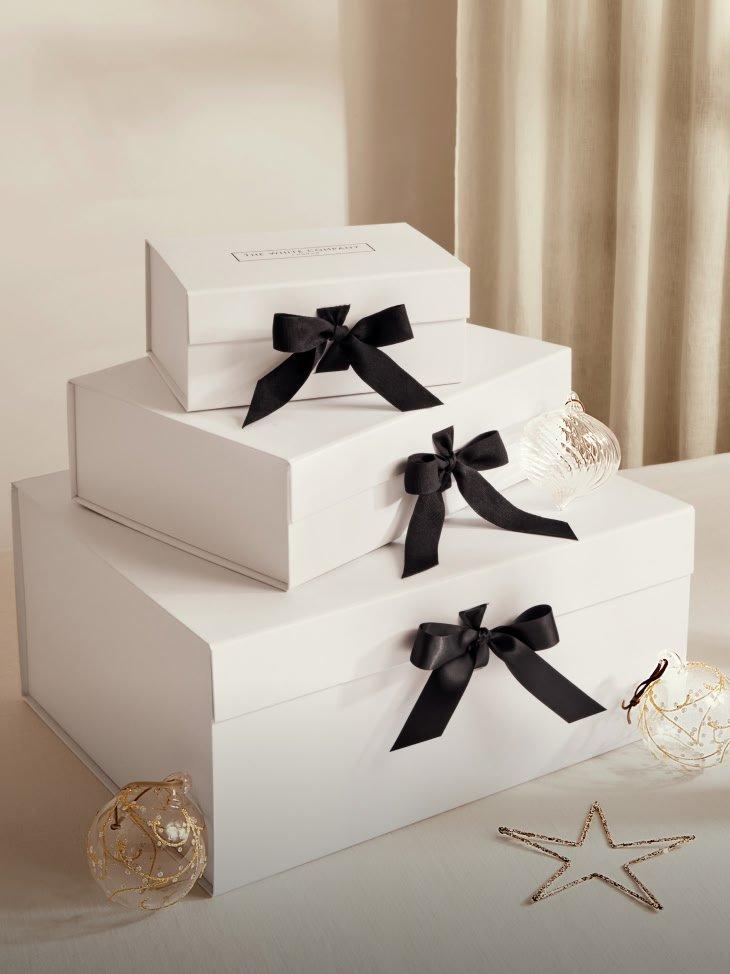 three white boxes with black bows on top of a table
