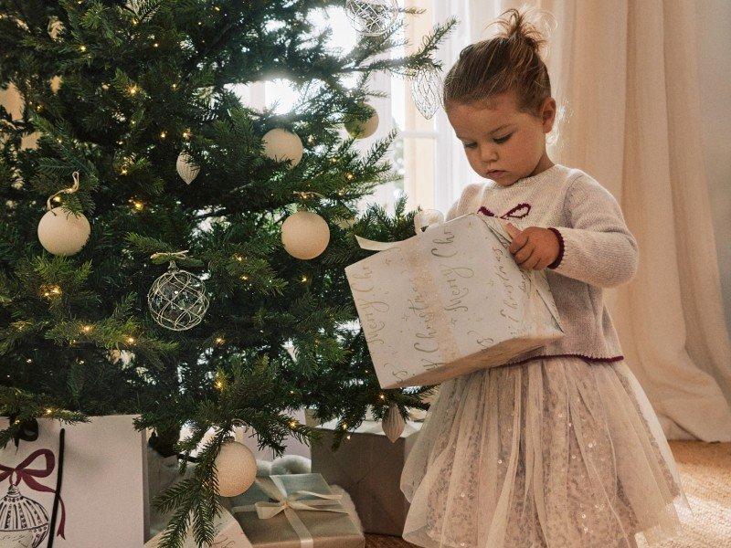 a little girl opening a gift under a christmas tree