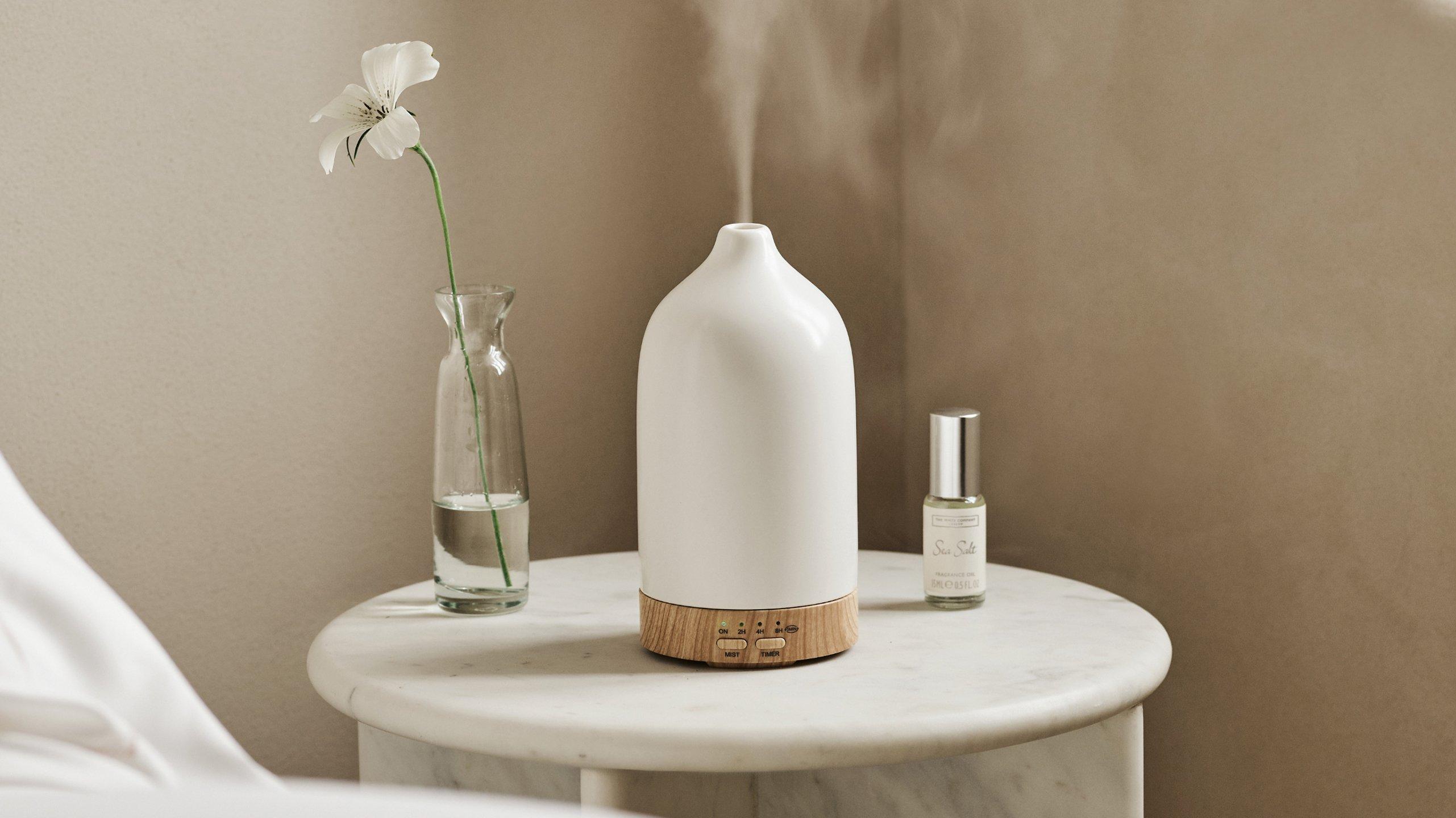 a white diffuser on a small table next to a vase of flowers
