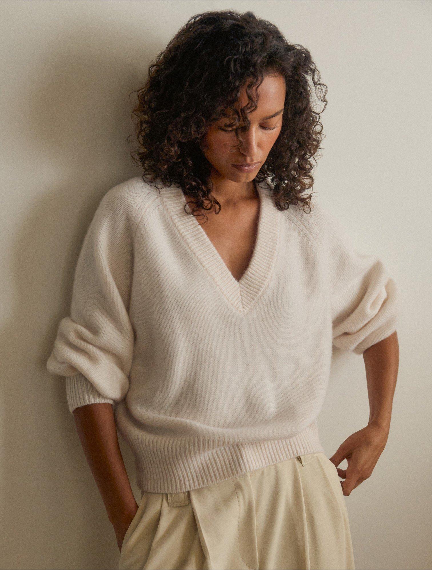 a woman in a white sweater leaning against a wall