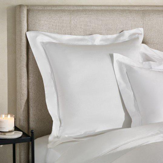 a bed with white sheets and pillows sitting next to a candle