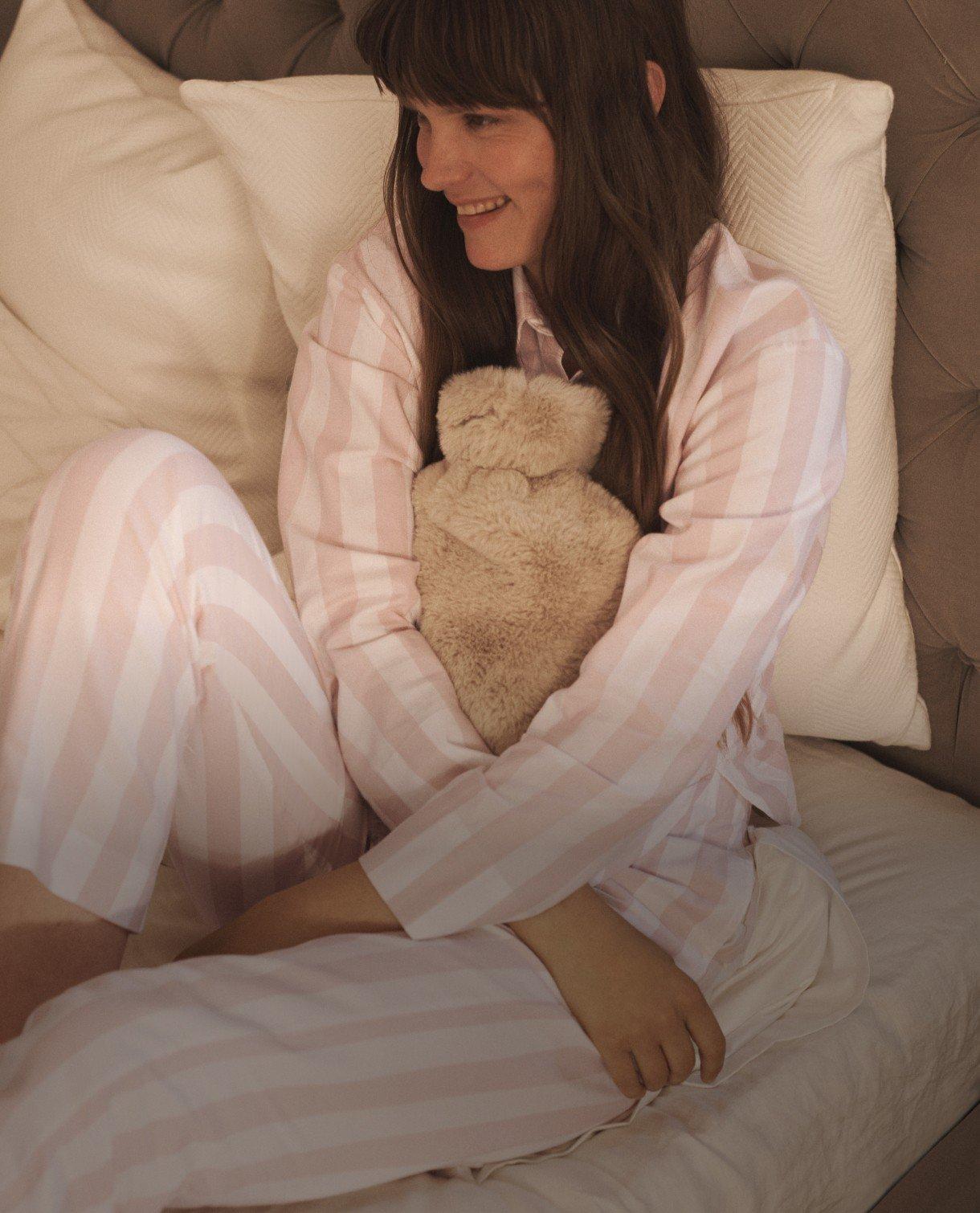 a woman in pajamas sitting on a bed holding a teddy bear