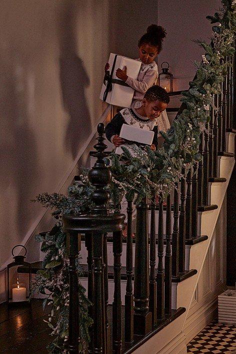 two children are climbing the stairs with presents under the tree