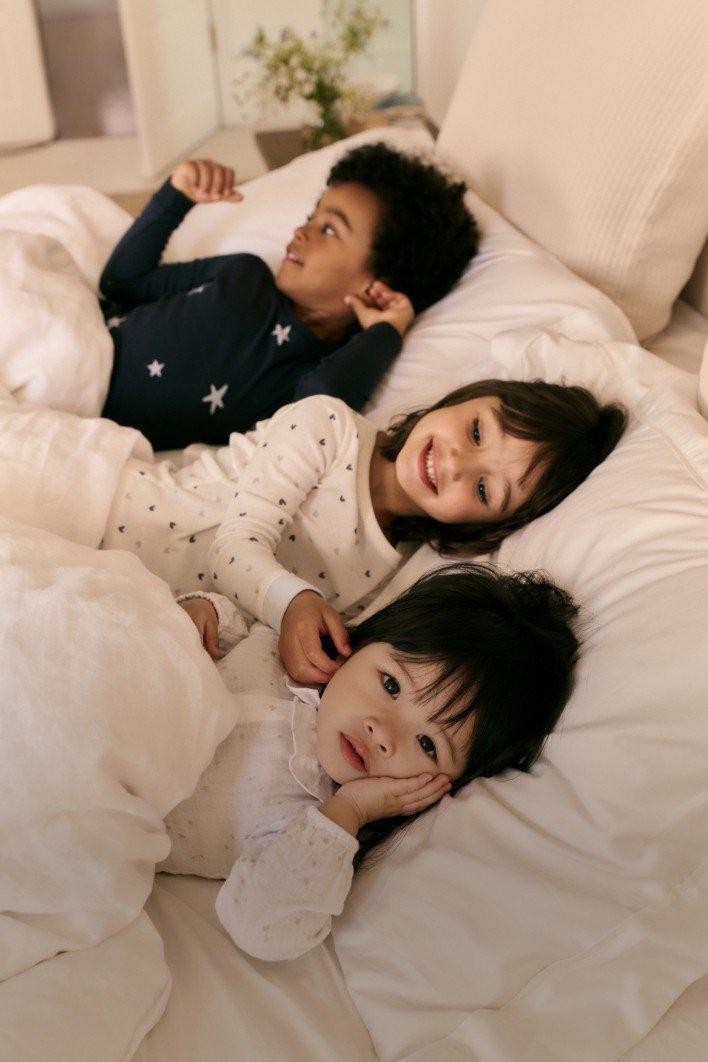 three children laying in a bed together with a white sheet