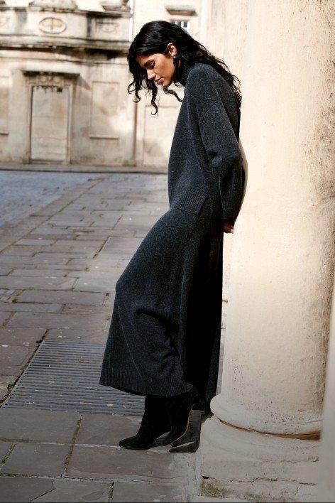 a woman leaning against a pillar in a long dress