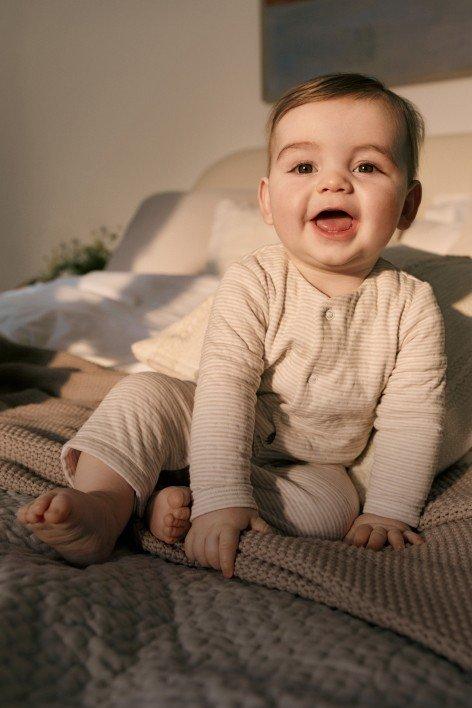 a little boy in a a sleepsuit sitting on a bed laughing