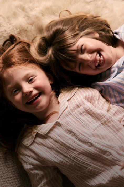 two little girls laying on a bed with a white fur blanket