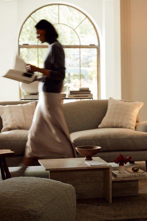 a woman walking in a room with a couch and a window