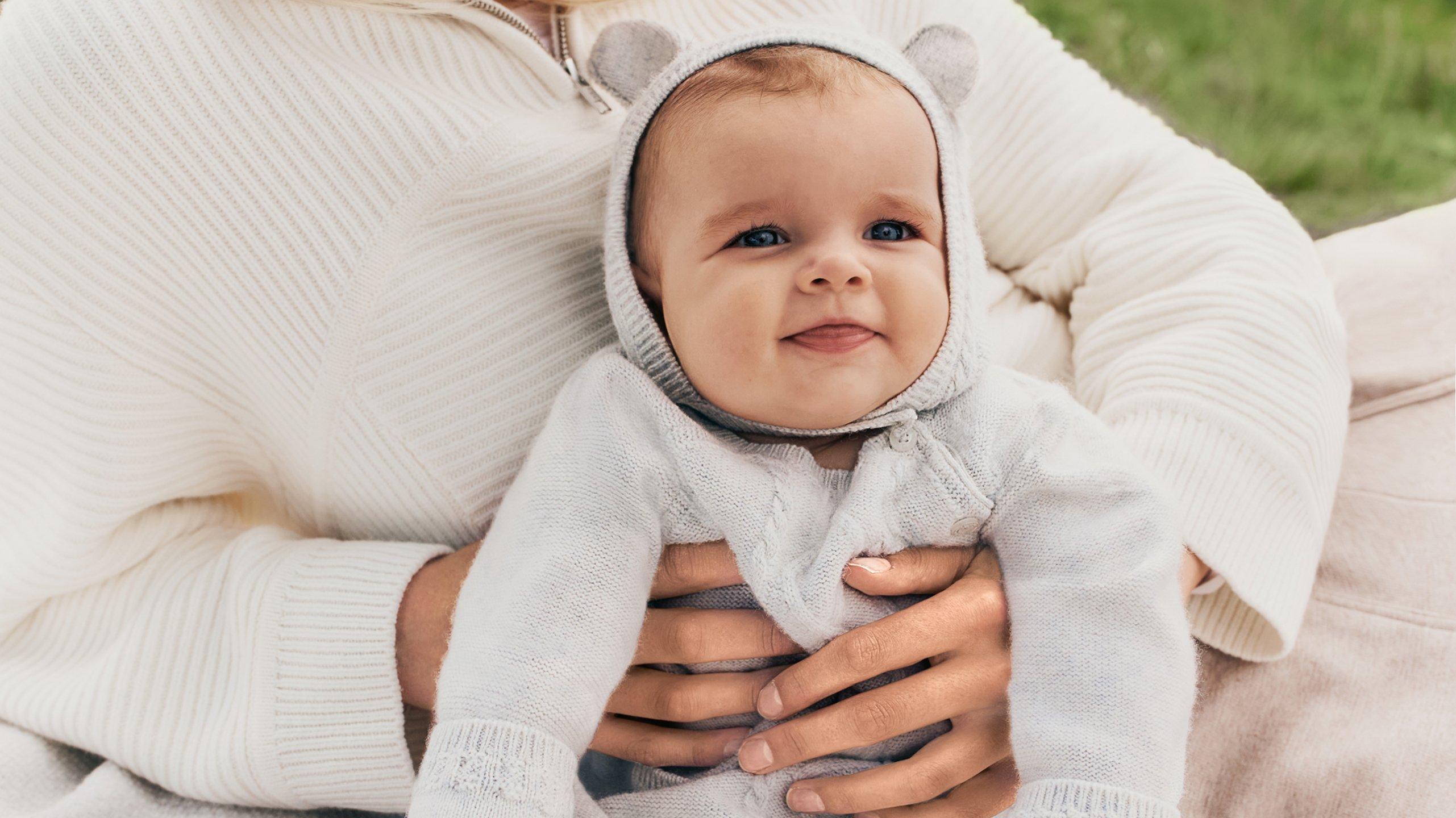 a woman holding a baby in her arms while wearing a sweater