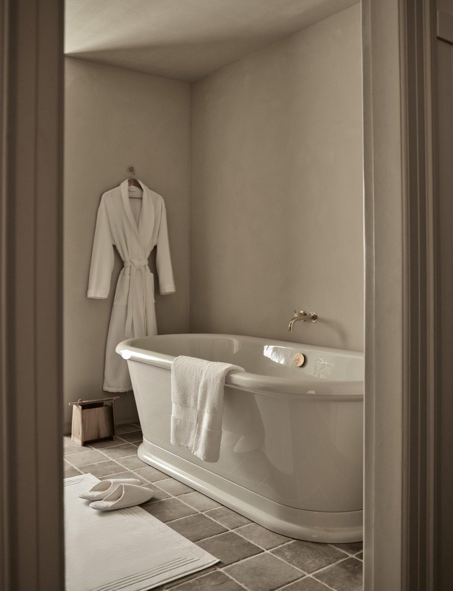 a bathtub in a bathroom with a robe hanging on the wall