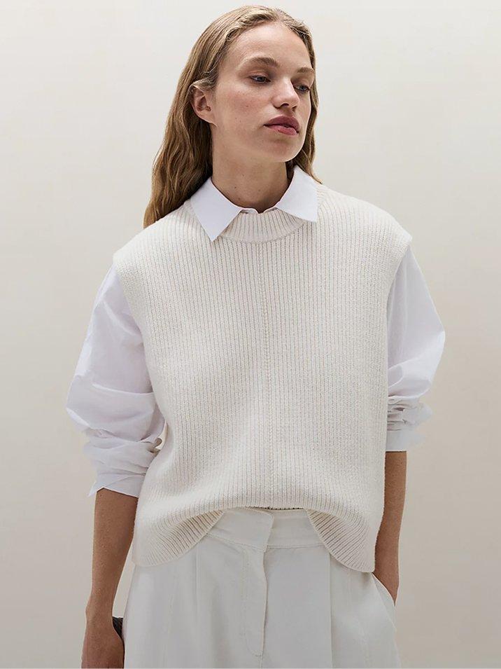 a woman in white pants and sweater standing with hands on hips