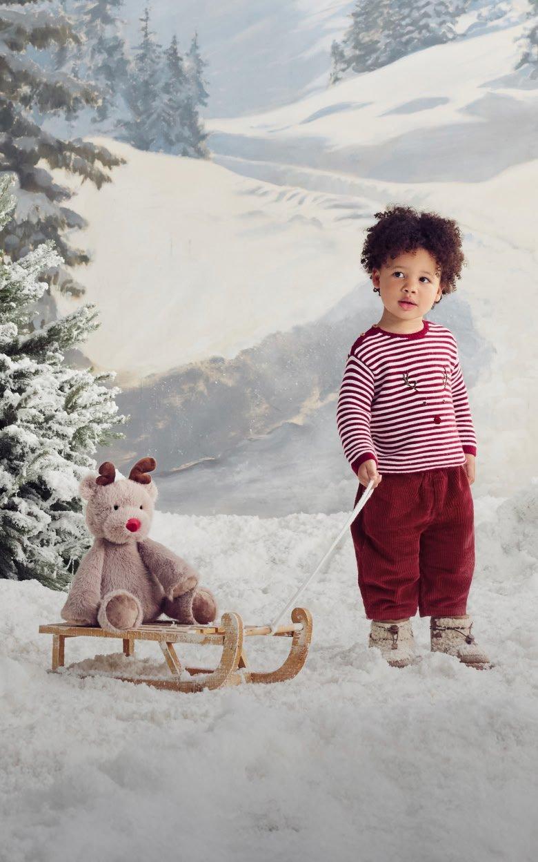 a young boy standing next to a teddy bear on a sled