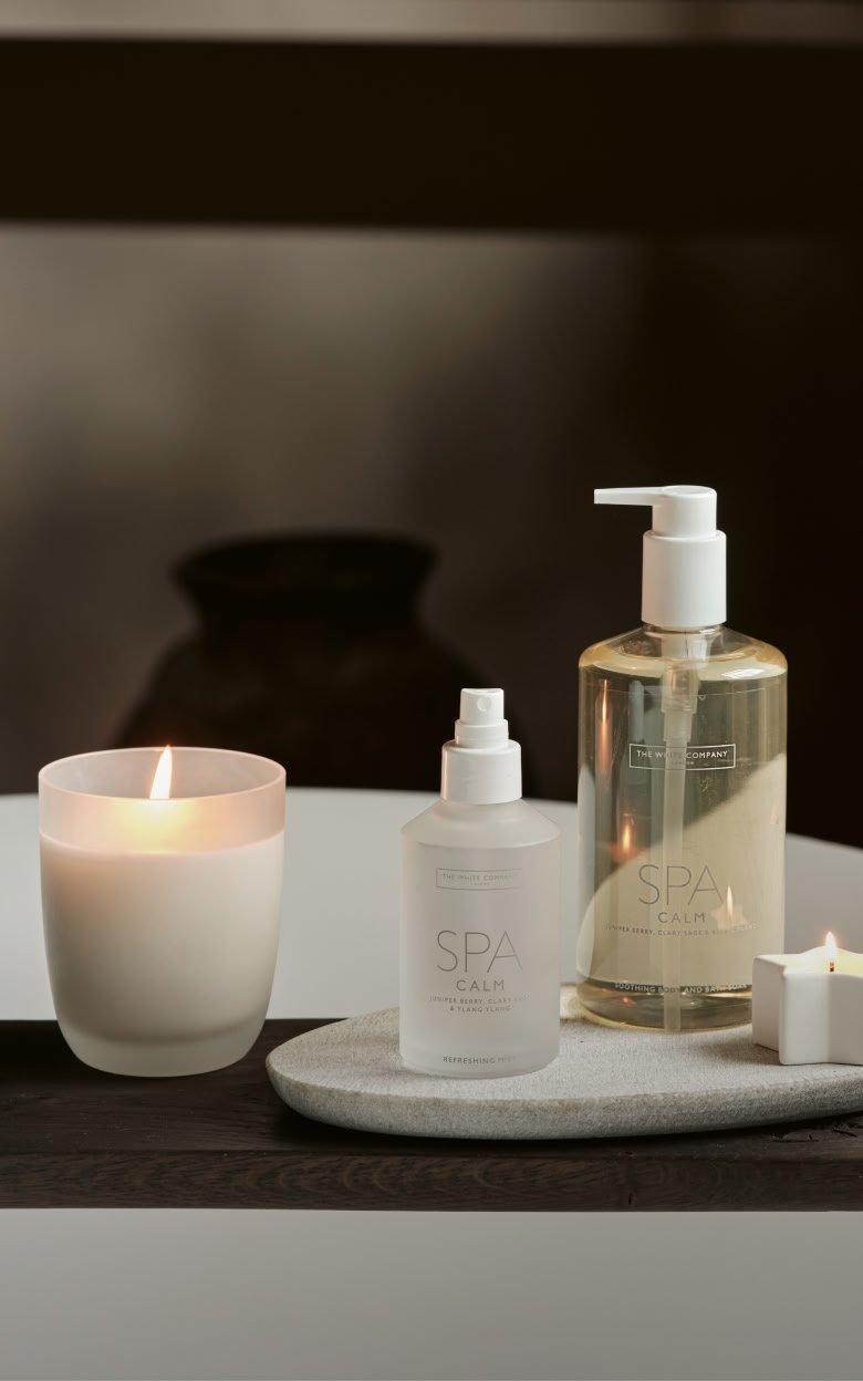 a white candle sitting on a white marble slab next to a bottle of lotion