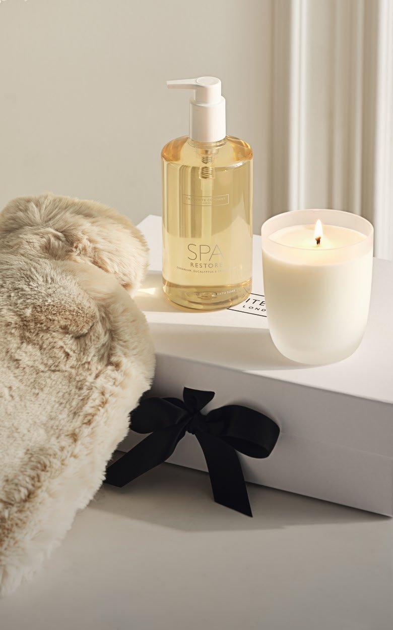 a candle and a bottle of lotion sit on a white table