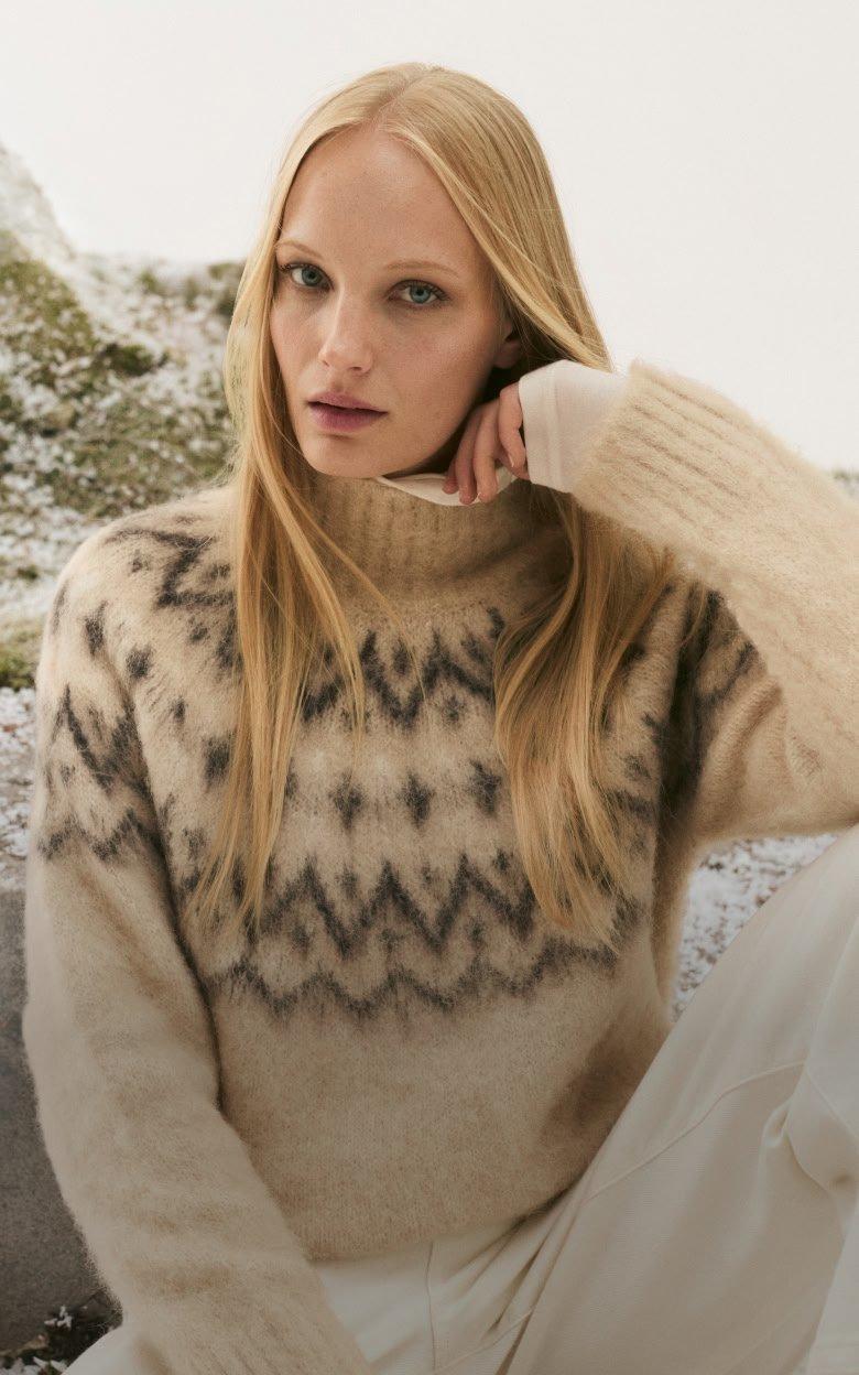 a woman in a sweater and pants sitting on a rock