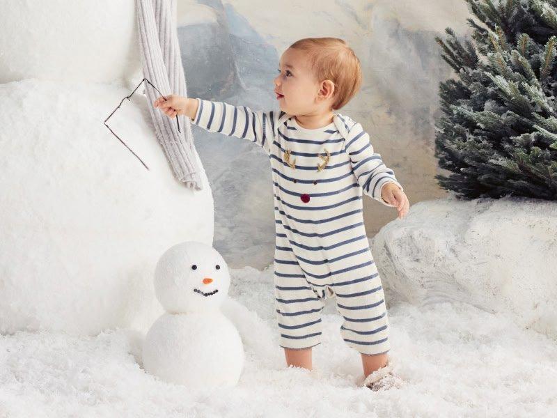 a baby in striped pajamas standing next to a snowman