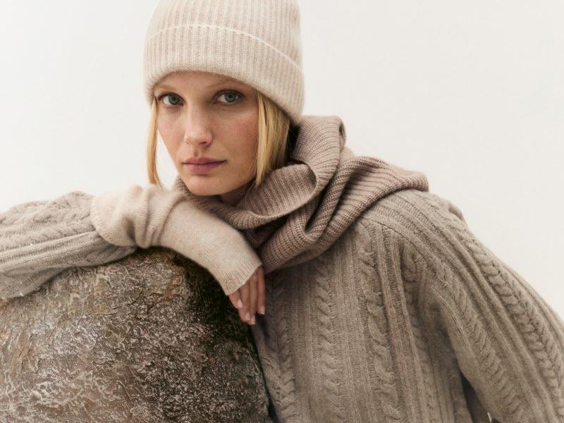 a woman in a hat and sweater leaning against a rock