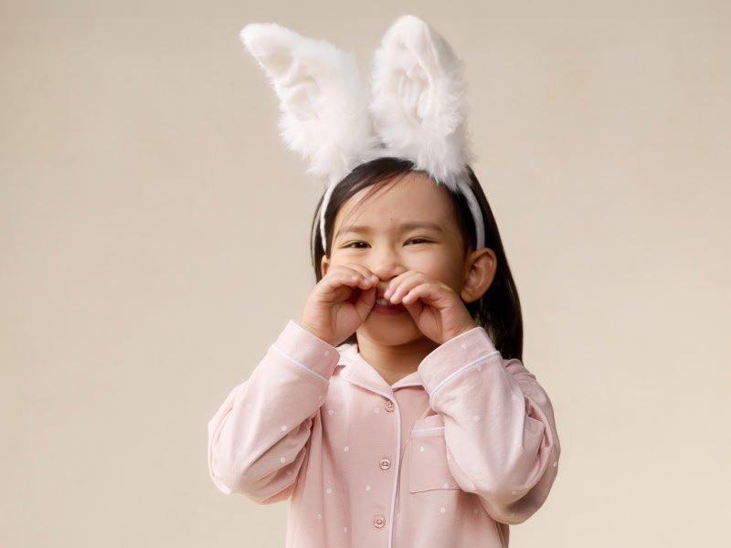 a little girl in pink pajamas with bunny ears on her head