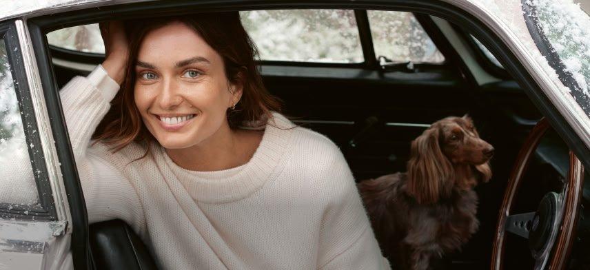 a woman in a white sweater sitting in a car with a dog
