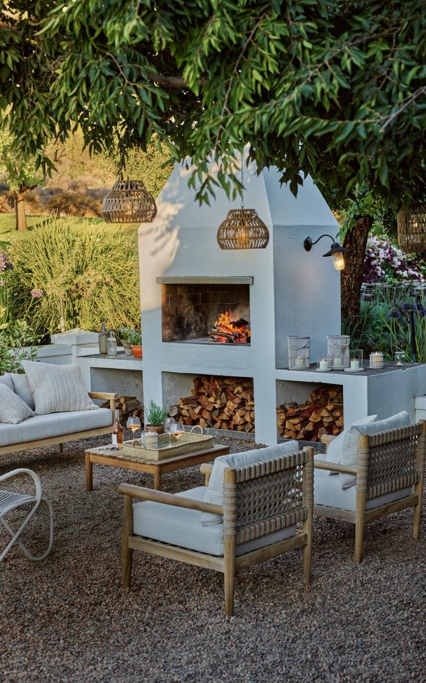 a white fireplace is surrounded by white furniture in a garden