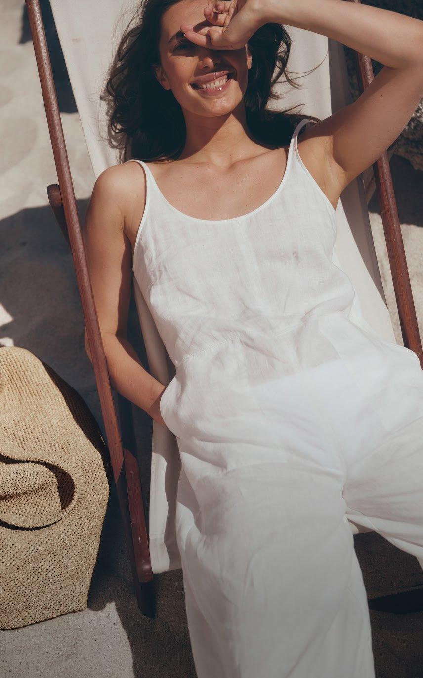 a woman in white jumpsuit laying in a chair with sunglasses on