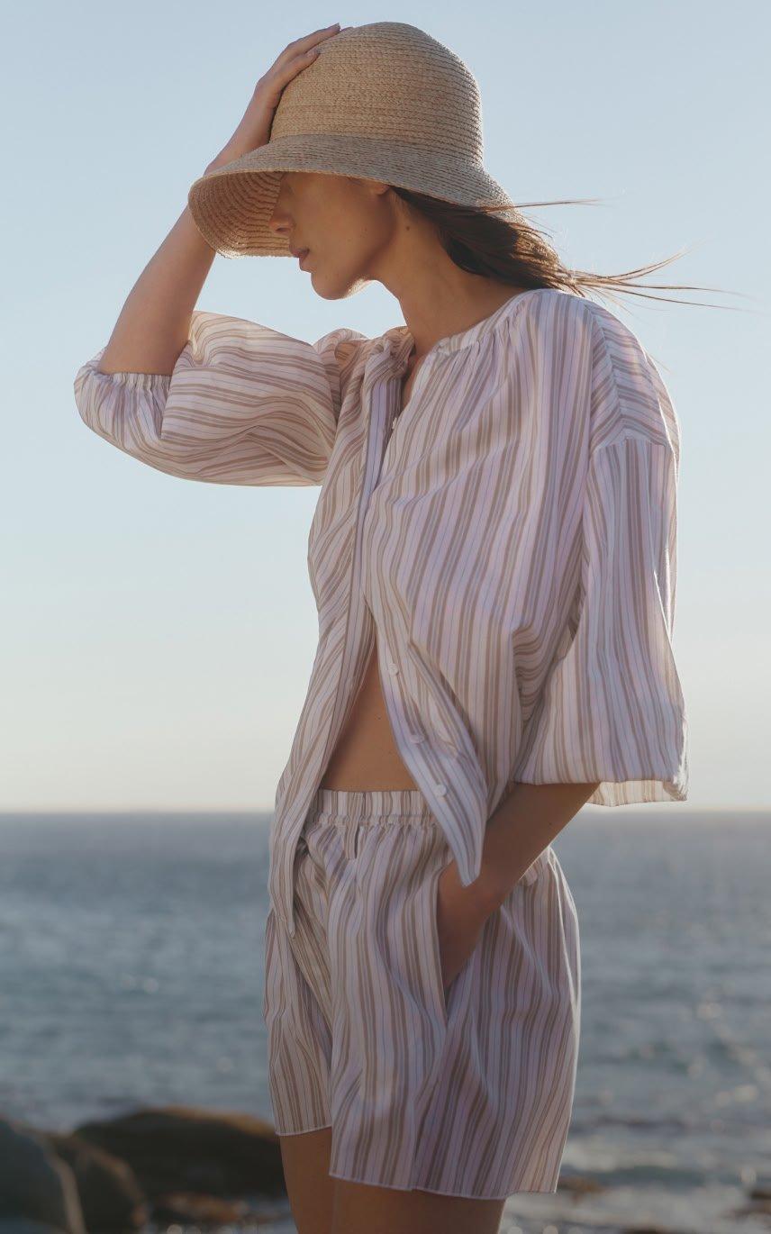 a woman in white jumpsuit standing on beach with bag